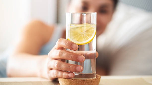 Glass of water with lemon slice in hand of woman